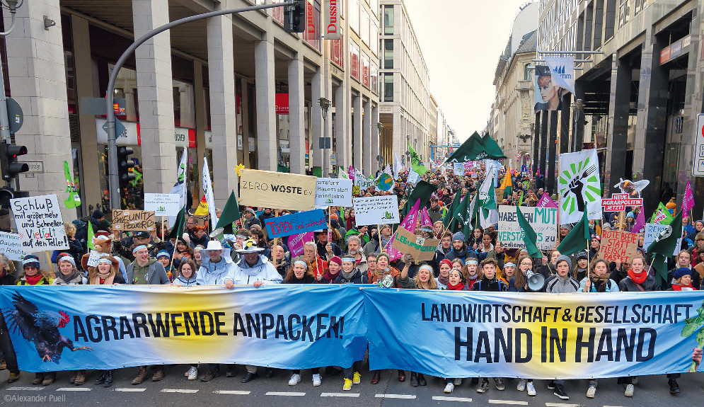 Eine große Gruppe Menschen demonstriert in Berlin auf der Straße. Auf den Transparenten steht "Agrarwende anpacken" und "Landwirtschaft & Gesellschaft Hand in Hand"