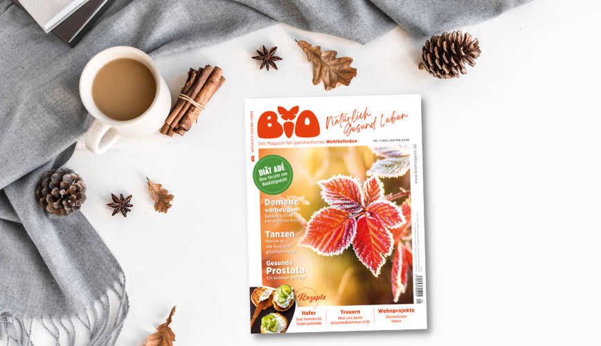 Die neue Ausgabe der Zeitschrift BIO liegt auf einem weißen Untergrund, umrahmt von einem grauen Schal, einer Tasse Kaffee, Zimtstangen und Tannenzapfen